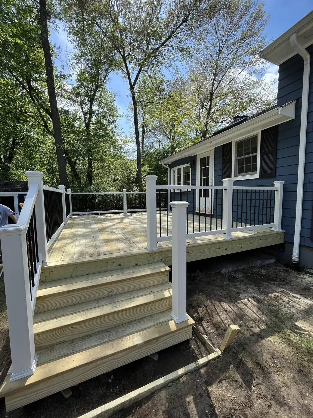 Newly framed pressure-treated deck with white railings and black balusters on a blue house