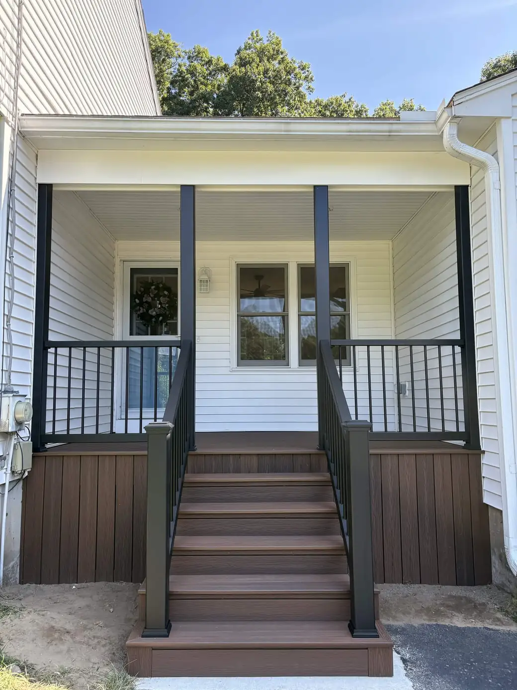 Covered entry porch with black posts, black railings and a brown composite deck