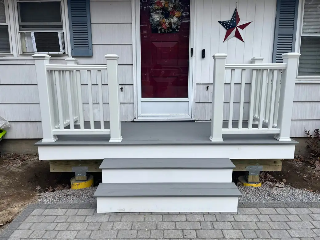 Small front porch on a ranch with grey composite decking, white railings and wide steps