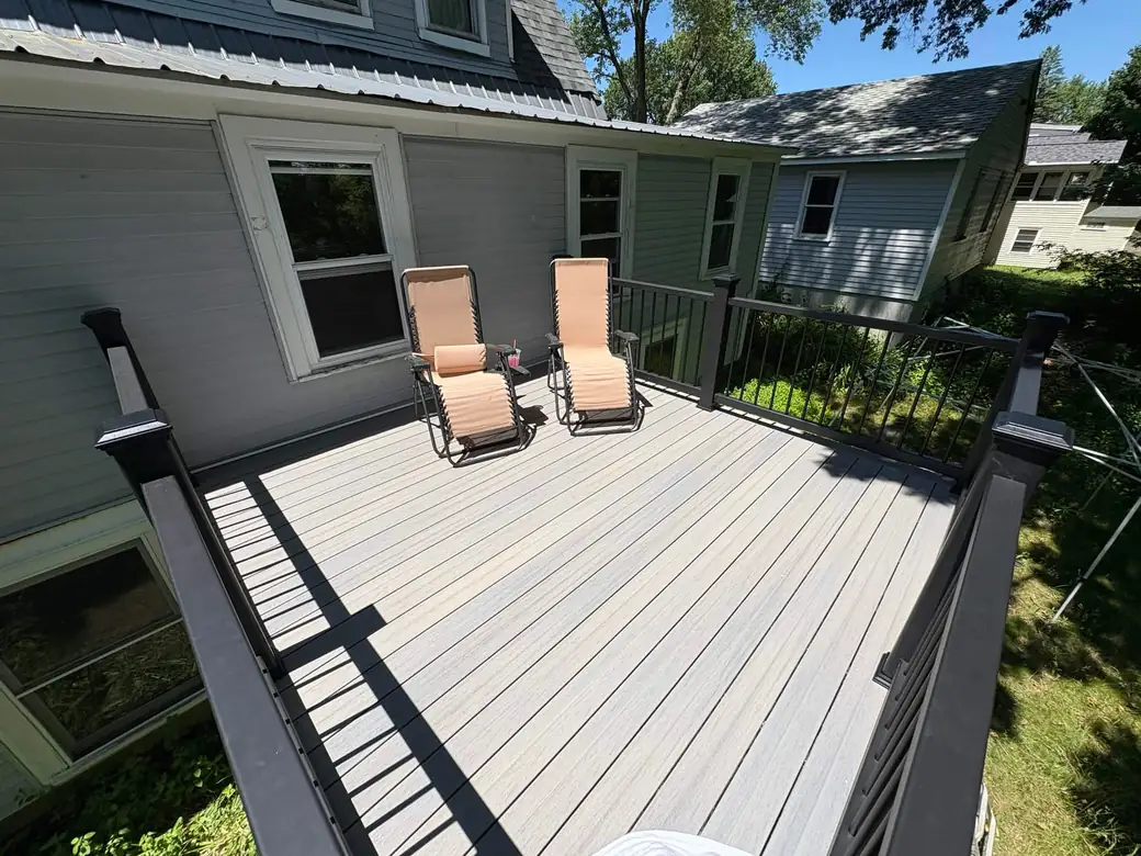 Raised backyard deck with grey composite boards and black aluminium railing on a sage-green house