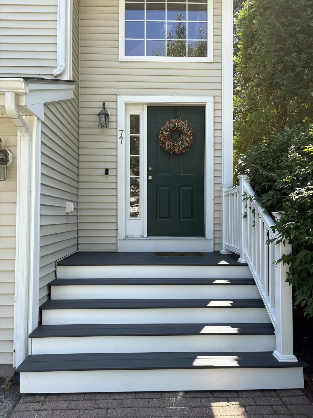 Four composite entry steps with dark grey treads and white risers leading to a green front door