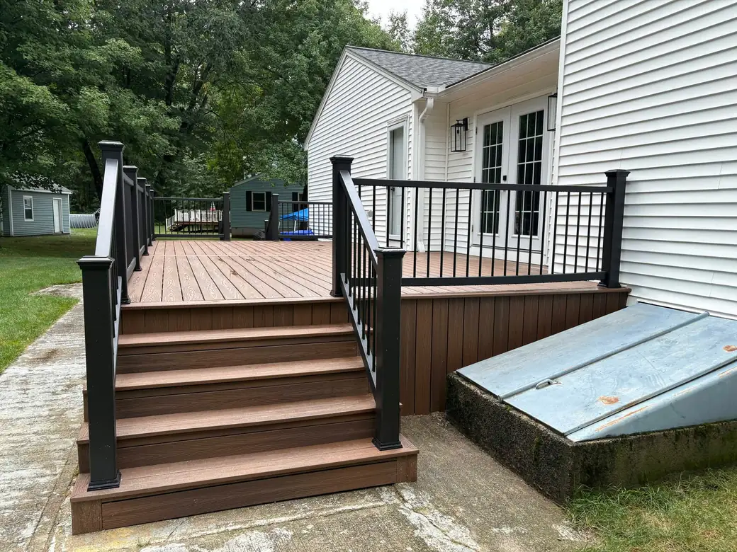 Full view of a backyard composite deck with black railings and centre stairs down to the lawn